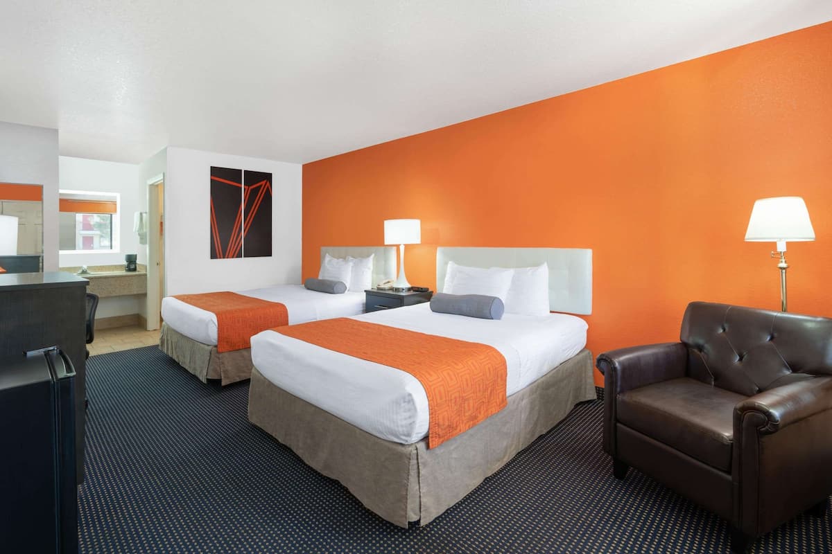 A hotel room with two beds, a desk, a chair, and a large orange accent wall.
