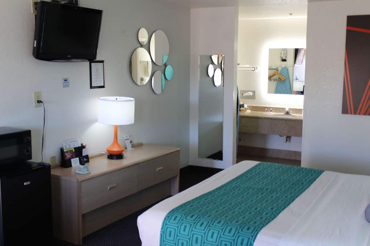 A hotel room with a bed, a desk with a lamp, a television, and a bathroom with a mirror and sink.