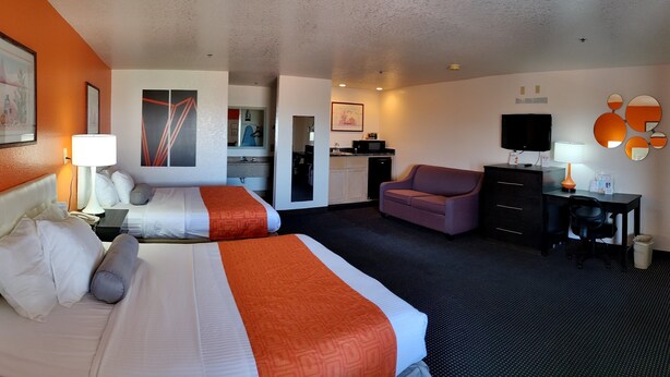 A hotel room with two beds, a desk, a chair, a TV, and a kitchenette.