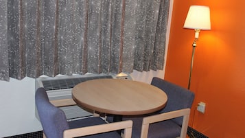 Um quarto com uma mesa redonda de madeira, duas cadeiras azuis, um abajur e uma janela com cortina.