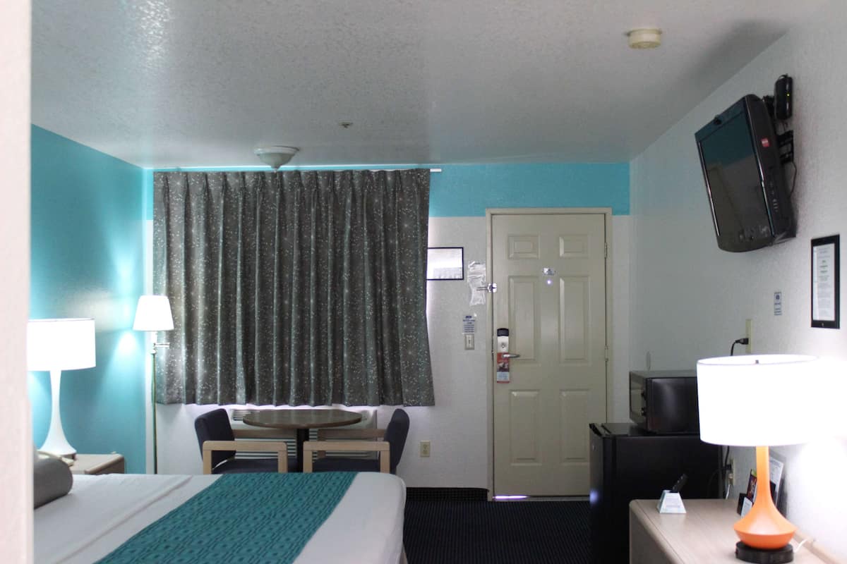 A hotel room with a bed, a desk, a chair, a television, and a door.