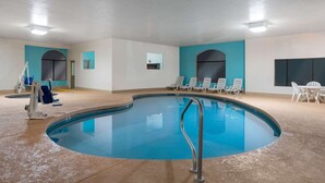 An indoor swimming pool with a clear water surface, surrounded by lounge chairs and a sunbed.