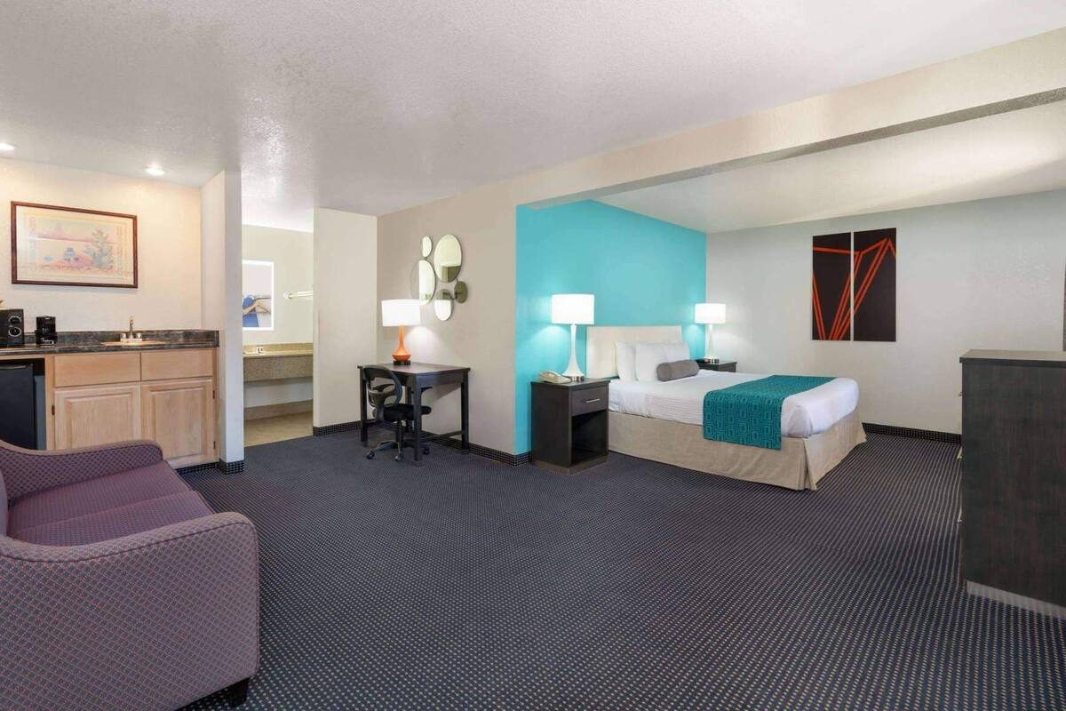 A hotel room with a bed, desk, chair, kitchenette, and a bathroom.