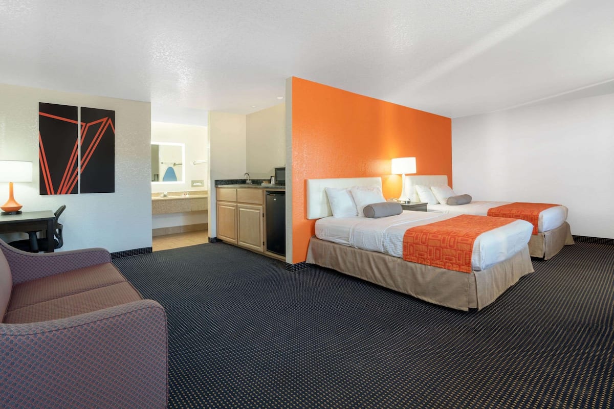 A hotel room with two beds, a desk, and a kitchenette.
