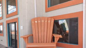 A wooden Adirondack chair with "I ♥ HOJO!" written on it, placed outside a building with orange trim and large windows.
