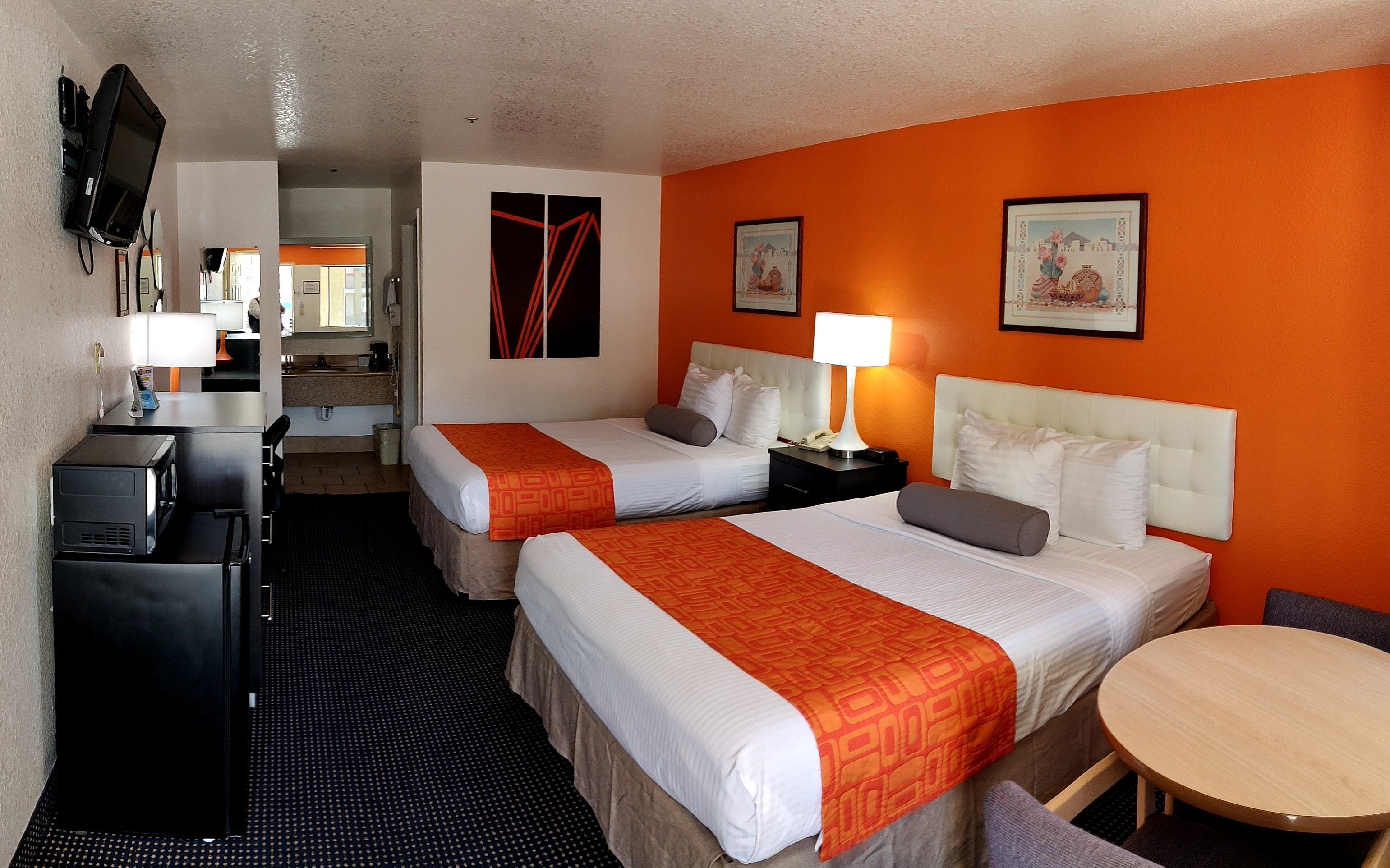 A hotel room with two beds, a desk, a chair, a round table, and a TV mounted on the wall.