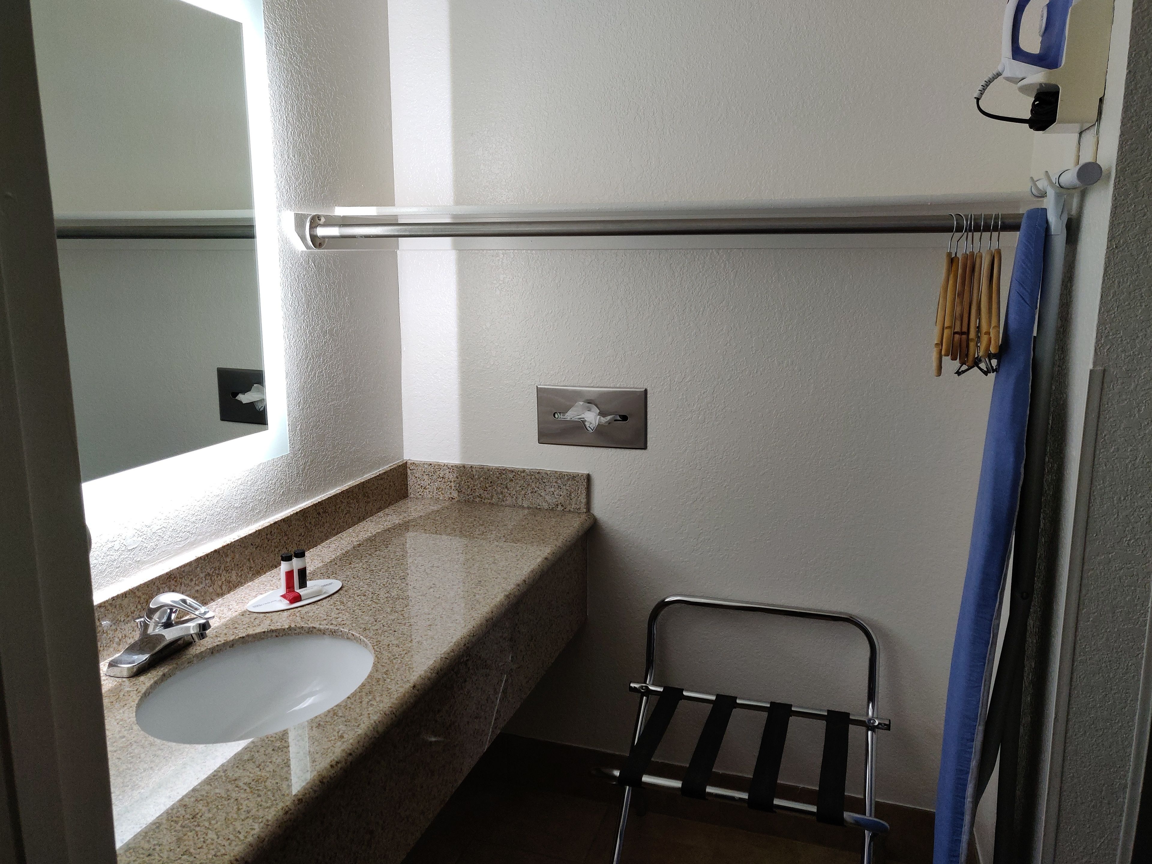 A bathroom with a granite countertop sink, a mirror, a towel rack, and a shower curtain.