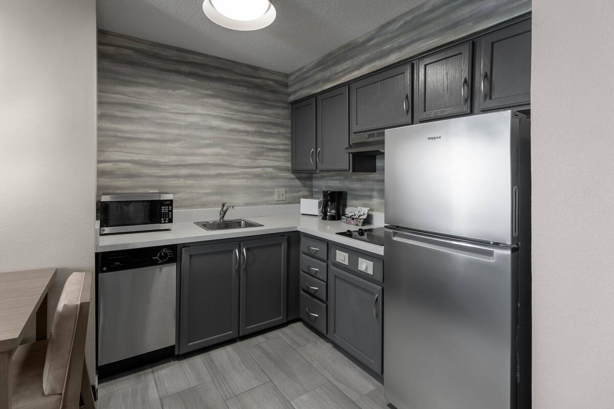A modern kitchen with grey cabinets, a stainless steel refrigerator, a microwave, and a dishwasher.