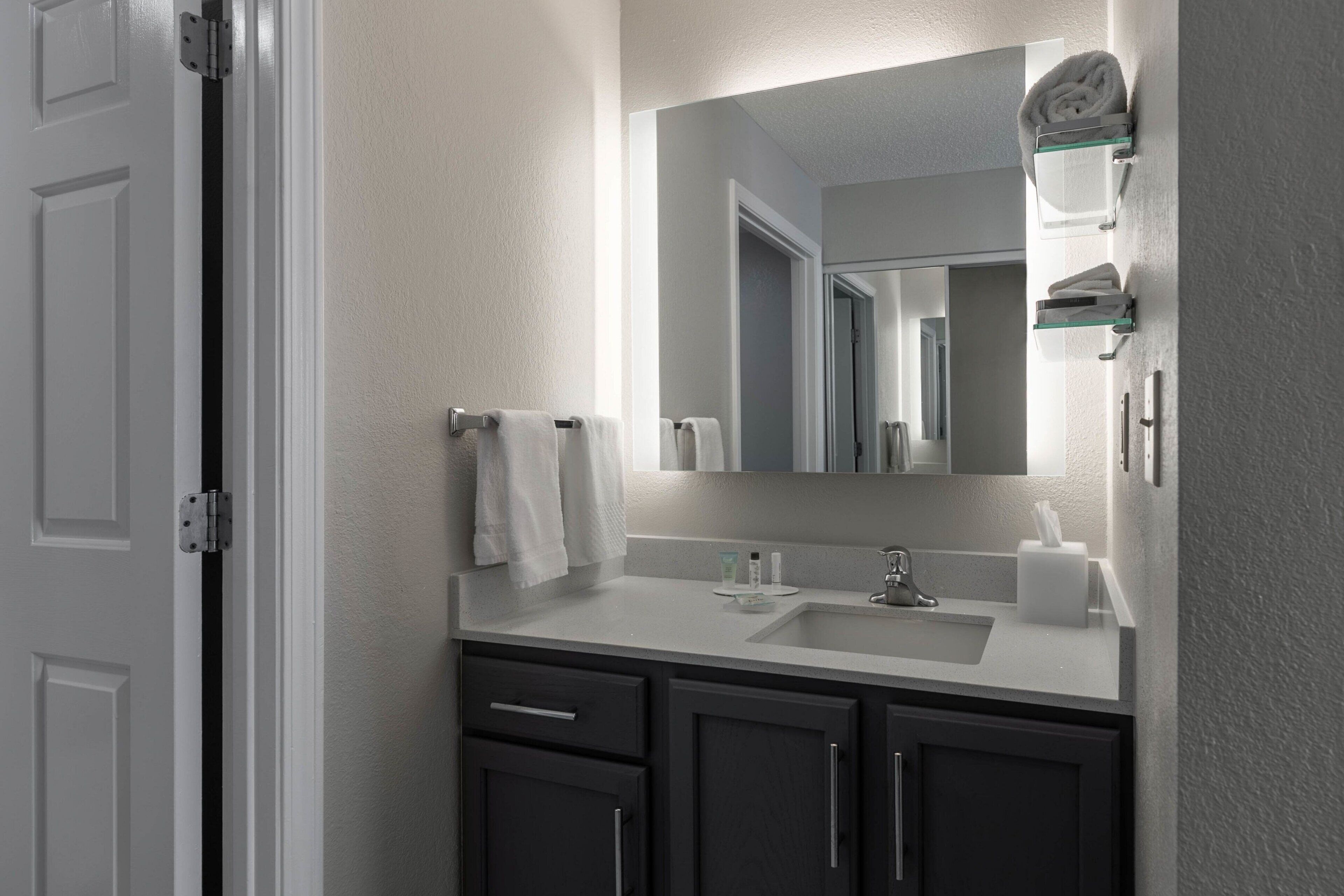 A bathroom with a white sink, dark cabinets, a mirror, and a towel rack.