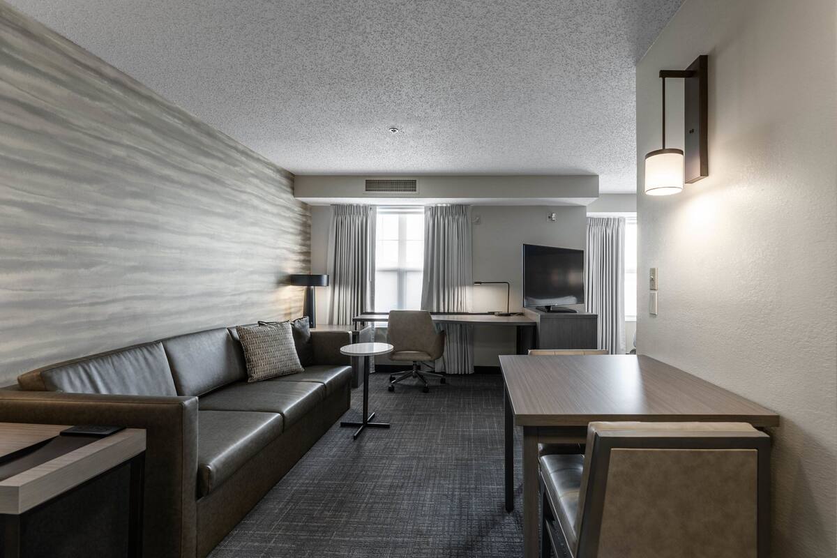A hotel room with a sofa, a small table, a desk, and a TV.