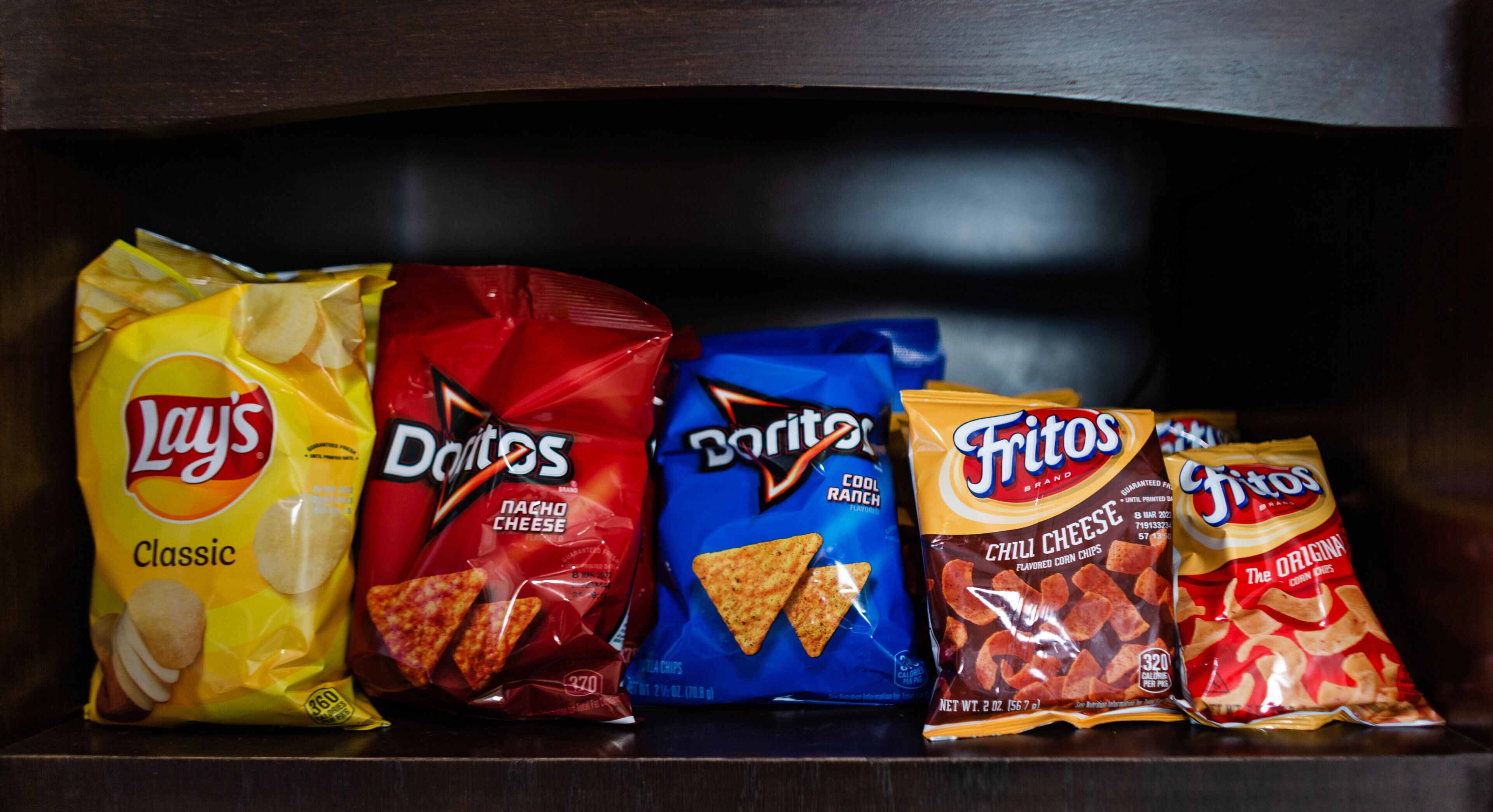 A shelf with bags of Lay's Classic, Doritos, and Fritos chips.