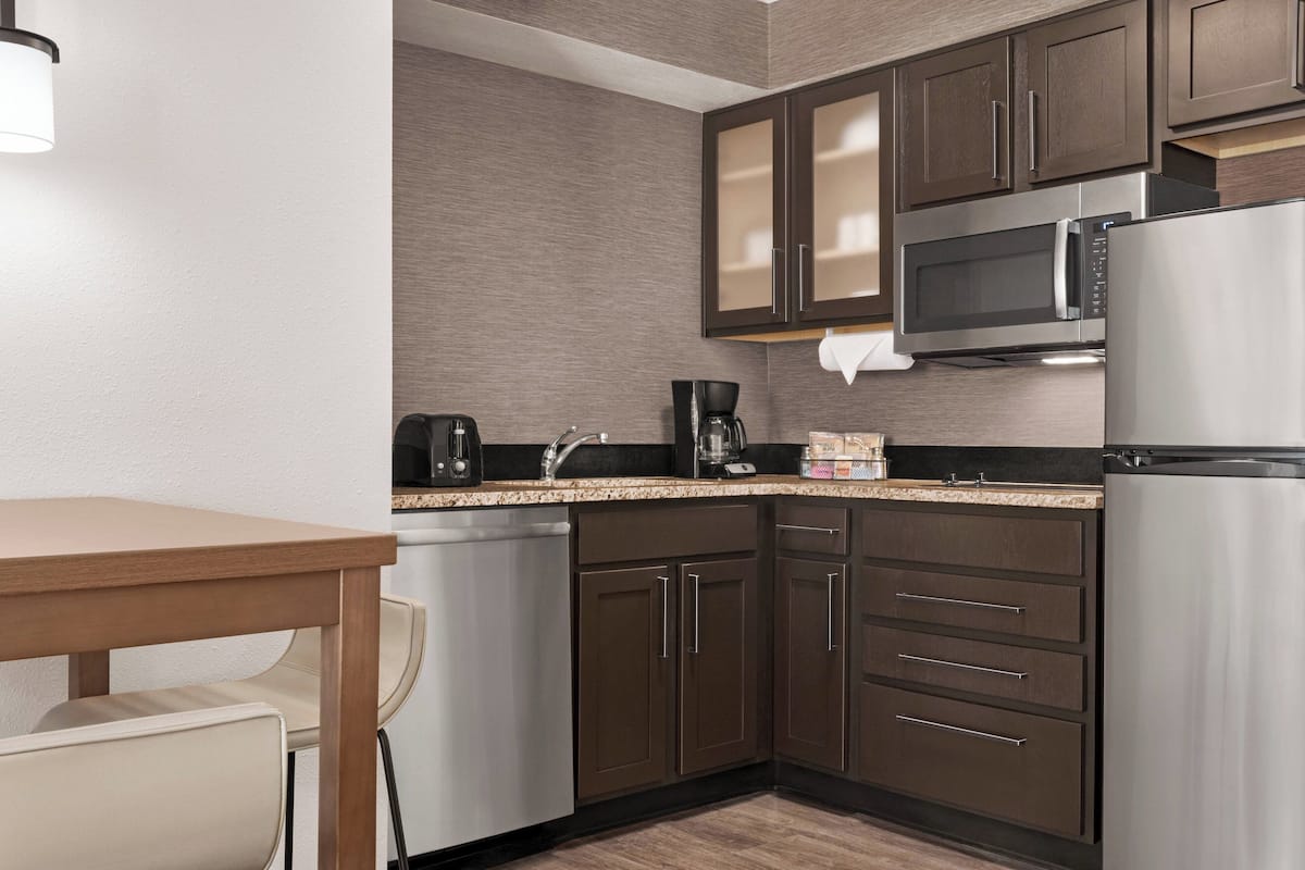 A modern kitchen with dark brown cabinets, stainless steel appliances, a wooden table, and a white chair.