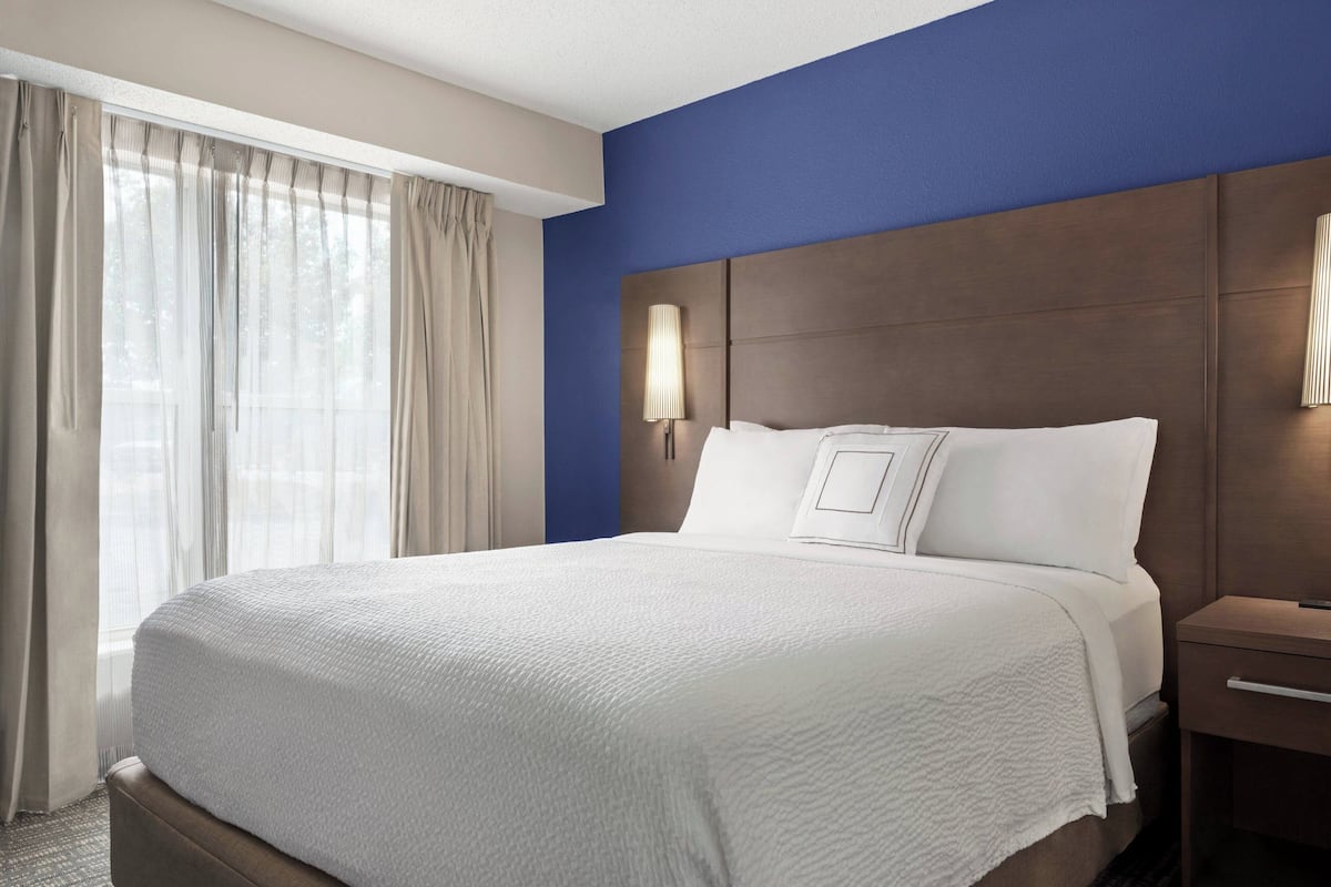 A hotel room with a large bed, a nightstand, a lamp, and a window with curtains.