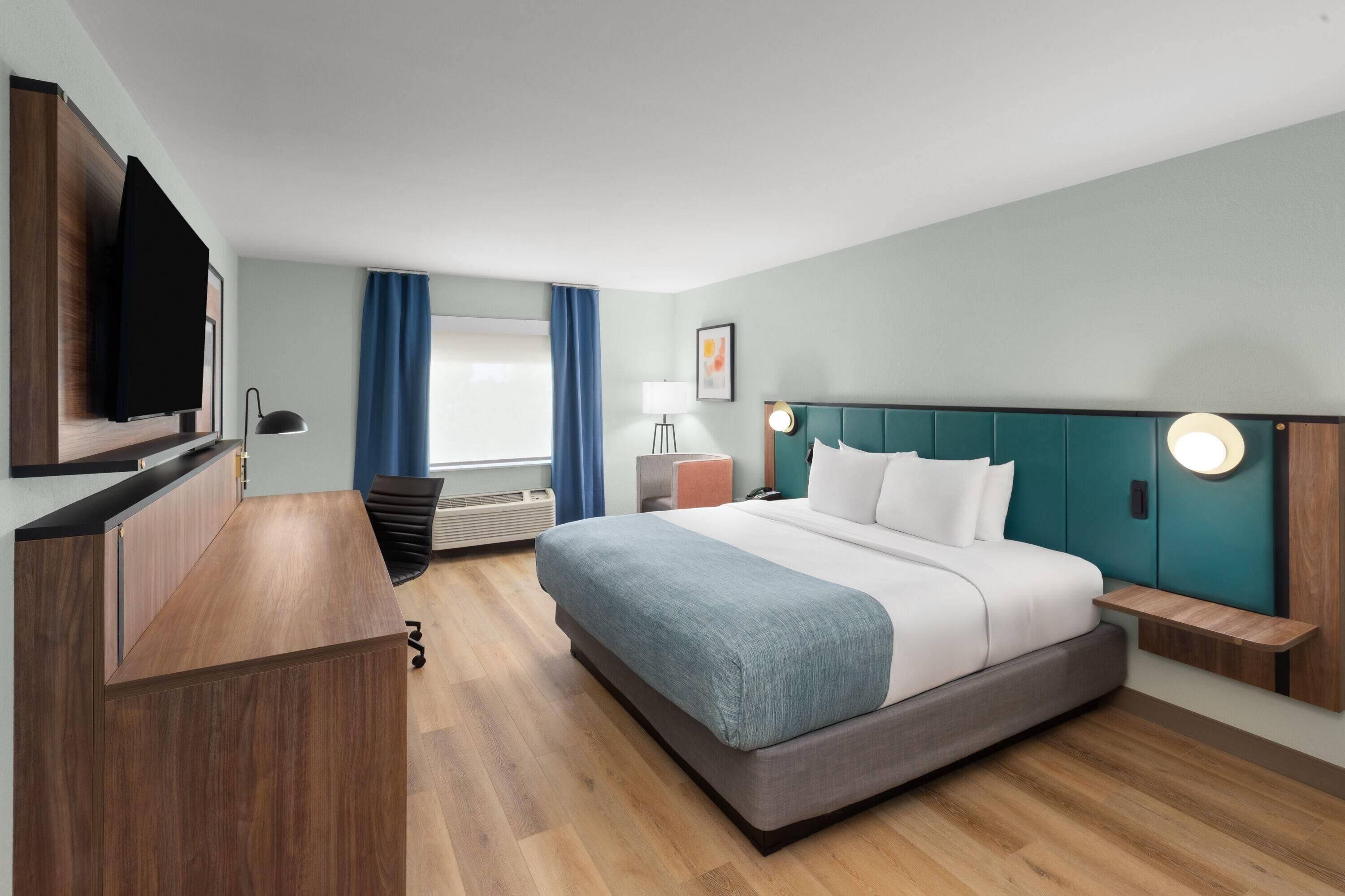 Une chambre d’hôtel moderne dotée d’un grand lit, d’un bureau, d’une télévision à écran plat et d’une fenêtre avec des rideaux.