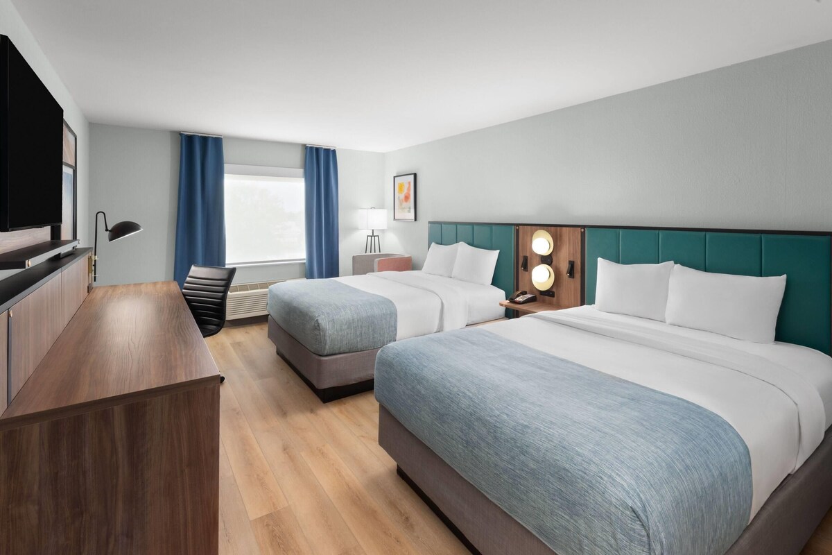 Una camera d'albergo con due letti, una scrivania, una TV e una finestra con tende.
