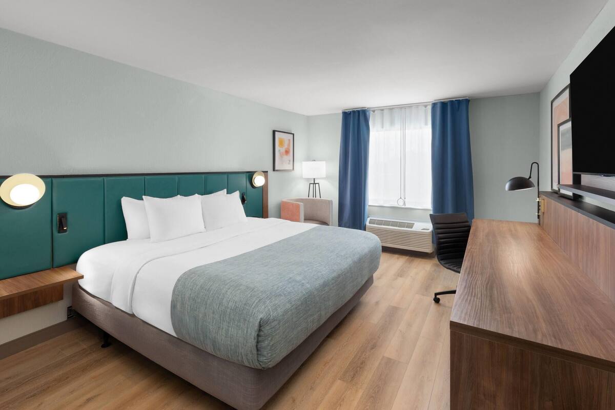 Ein Hotelzimmer mit Bett, Nachttisch, Schreibtisch, Stuhl, Lampe und Fernseher.