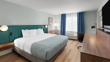 A hotel room with a bed, bedside table, desk, chair, lamp, and a TV.