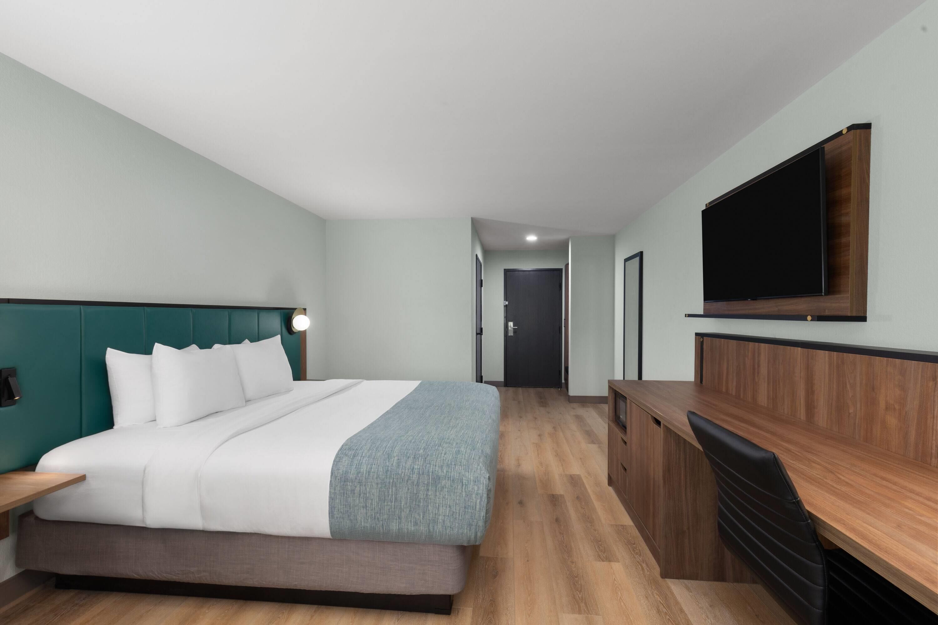 Una habitación de hotel moderna con una cama, un escritorio y un televisor de pantalla plana montado en la pared.