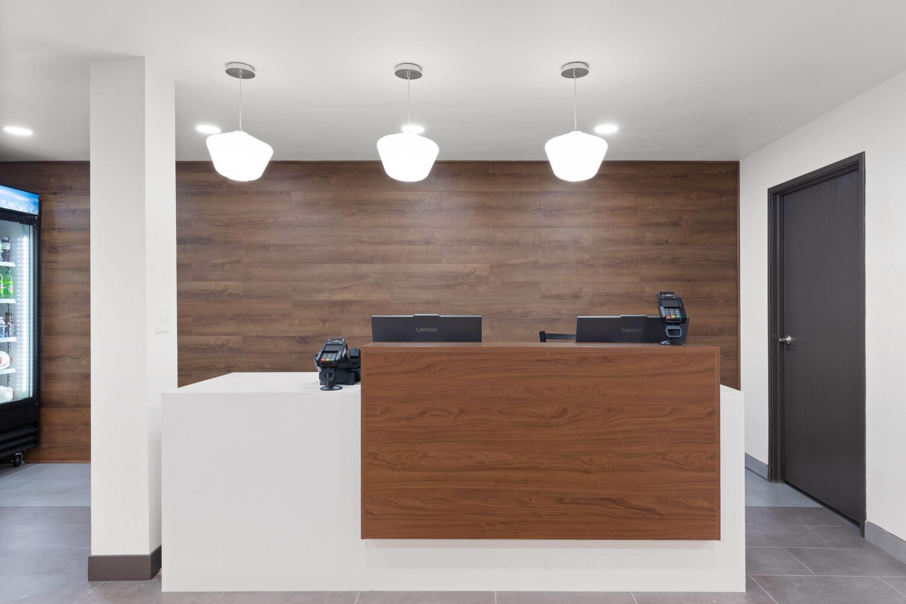 A reception desk with a wooden panel, two computers, a phone, and a cash register.
