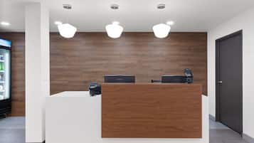 Un mostrador de recepción con paneles de madera, dos computadoras, un teléfono y una caja registradora.