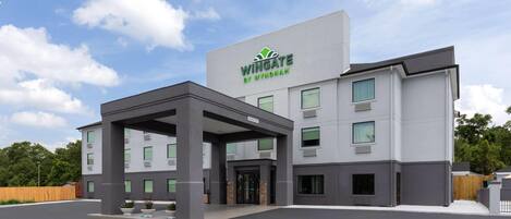 A modern building with a sign reading "Wingate by Wyndham." It features a covered entrance, multiple windows, and a parking lot.