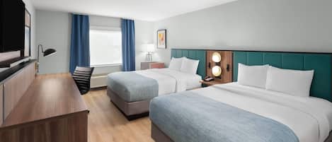 Quarto de hotel com duas camas, uma escrivaninha, televisão e janela com cortinas.