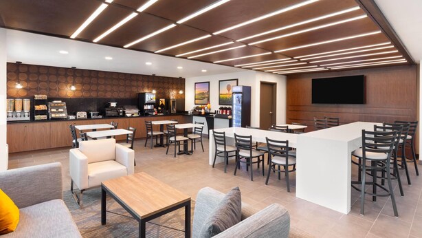 A modern bar area with a long counter, multiple seating options including bar stools and tables, and a television mounted on the wall. - Wingate by Wyndham Augusta I-20 (Augusta)
