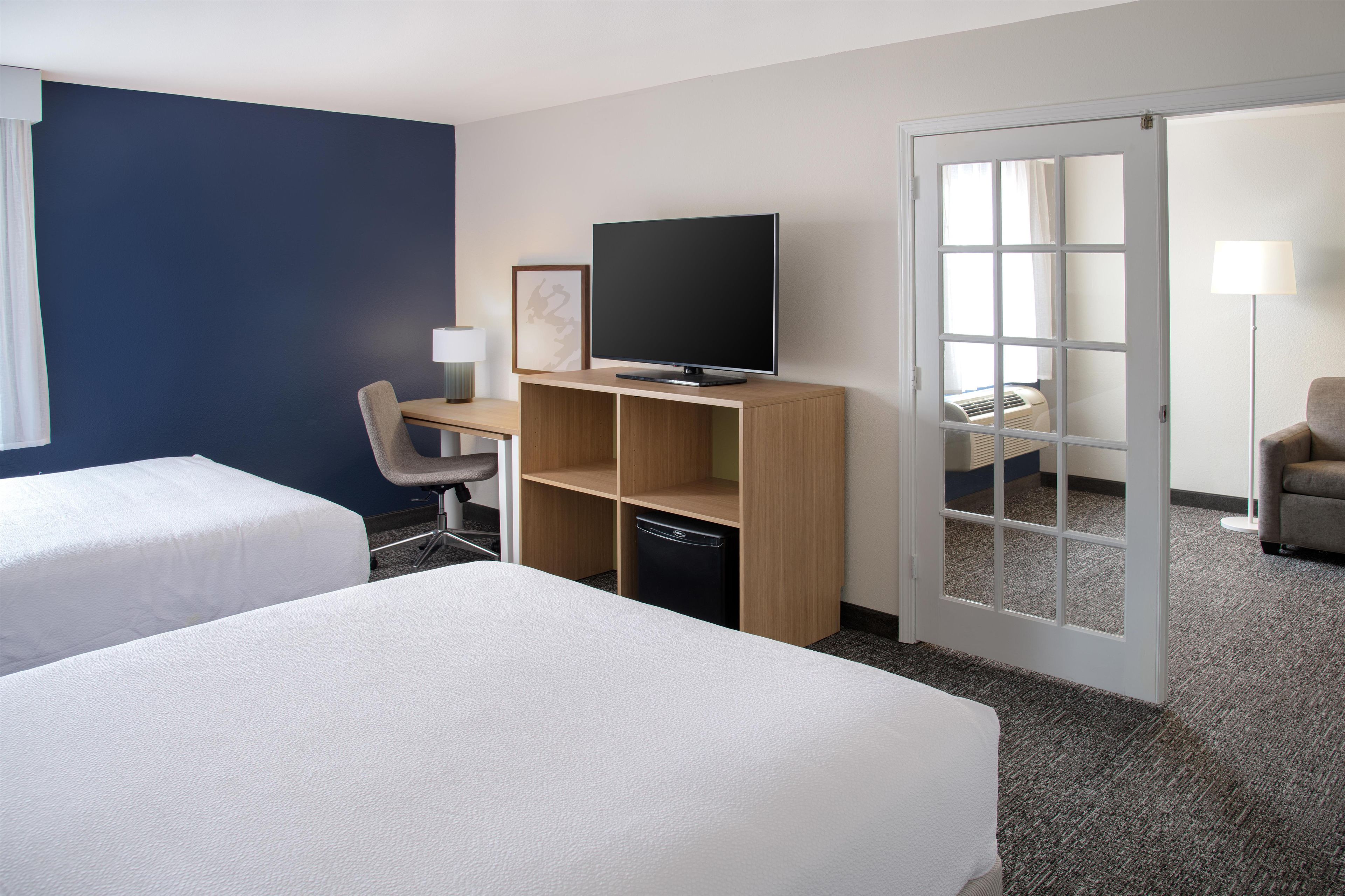 Une chambre d’hôtel avec deux lits, un bureau avec une télévision, une chaise et une porte donnant sur une autre pièce.