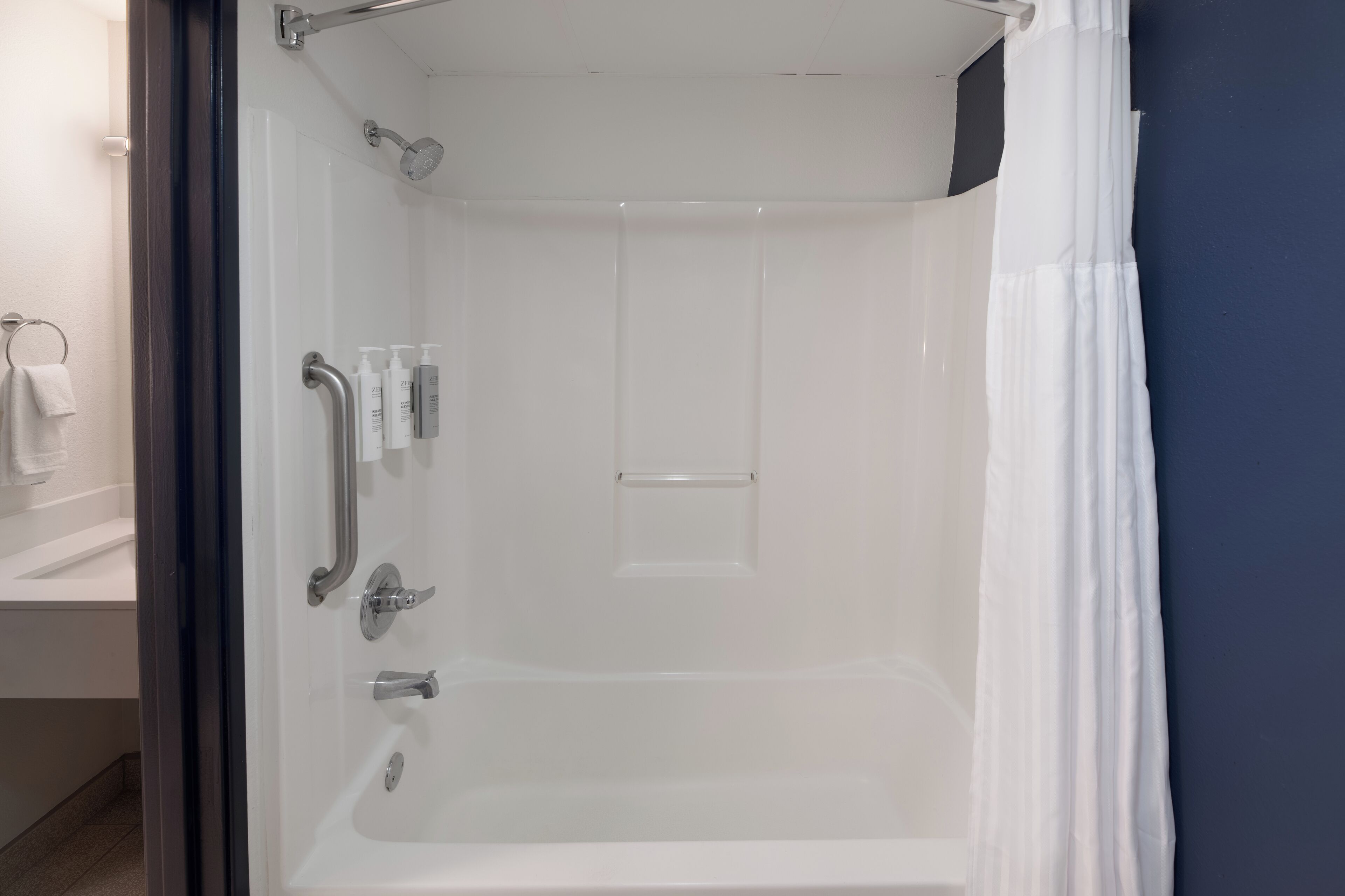 A modern bathroom with a glass shower enclosure, white fixtures, and a dark blue accent wall.