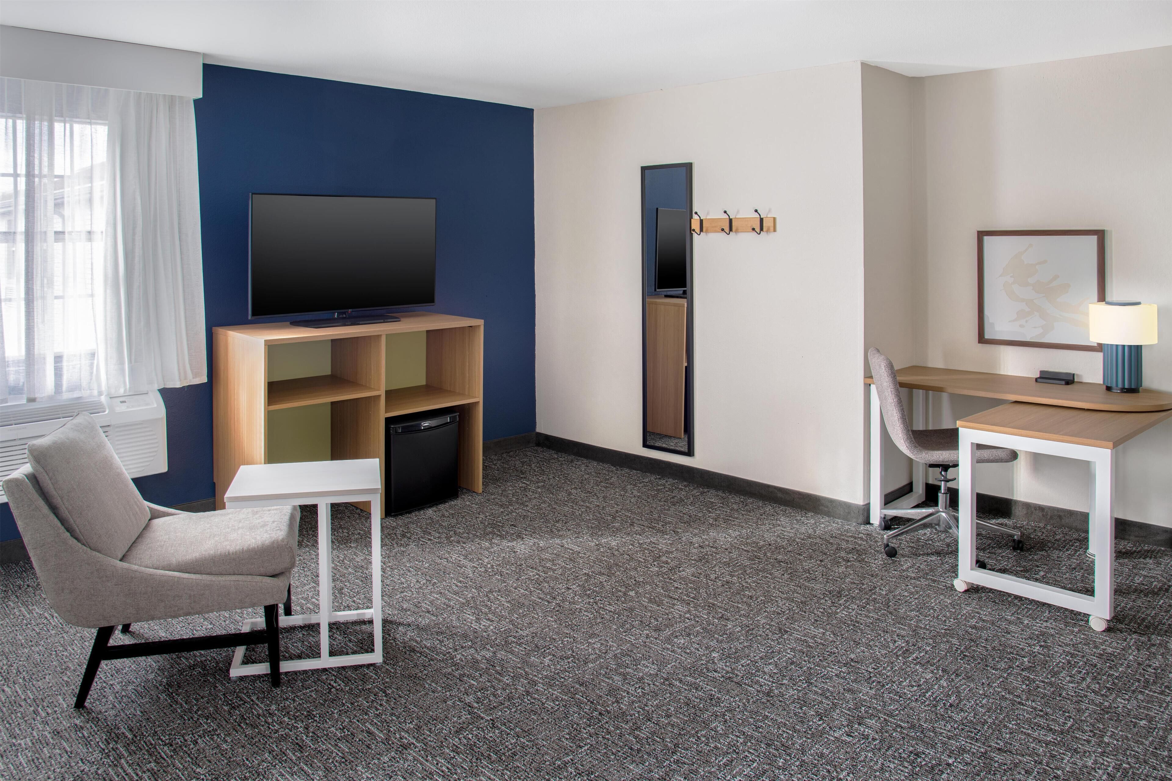 A hotel room with a flat-screen TV, a desk with a chair, a sofa, and a small table.