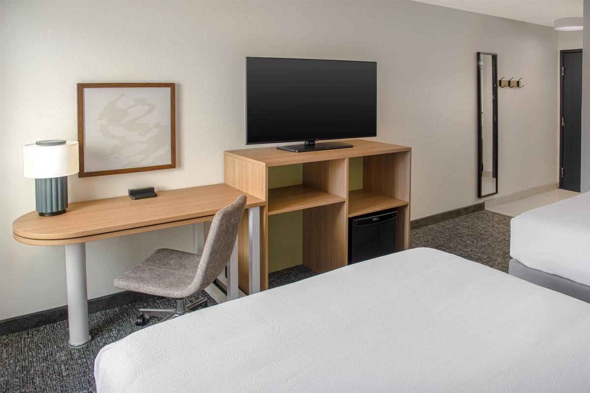 A hotel room with a wooden desk, a television, a chair, a bed, and a mirror.
