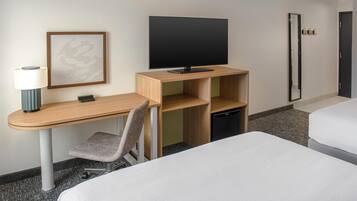 A hotel room with a wooden desk, a television, a chair, a bed, and a mirror.