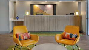 Un espace d’accueil au design moderne, comprenant un comptoir de réception, deux fauteuils à bascule jaunes avec des coussins colorés et une table ronde placée au centre.