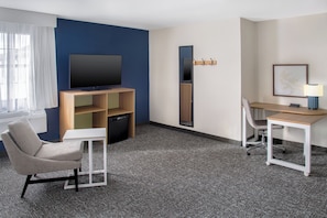 Een hotelkamer met een flatscreen televisie, een bureau met een stoel, een bank en een kleine tafel.