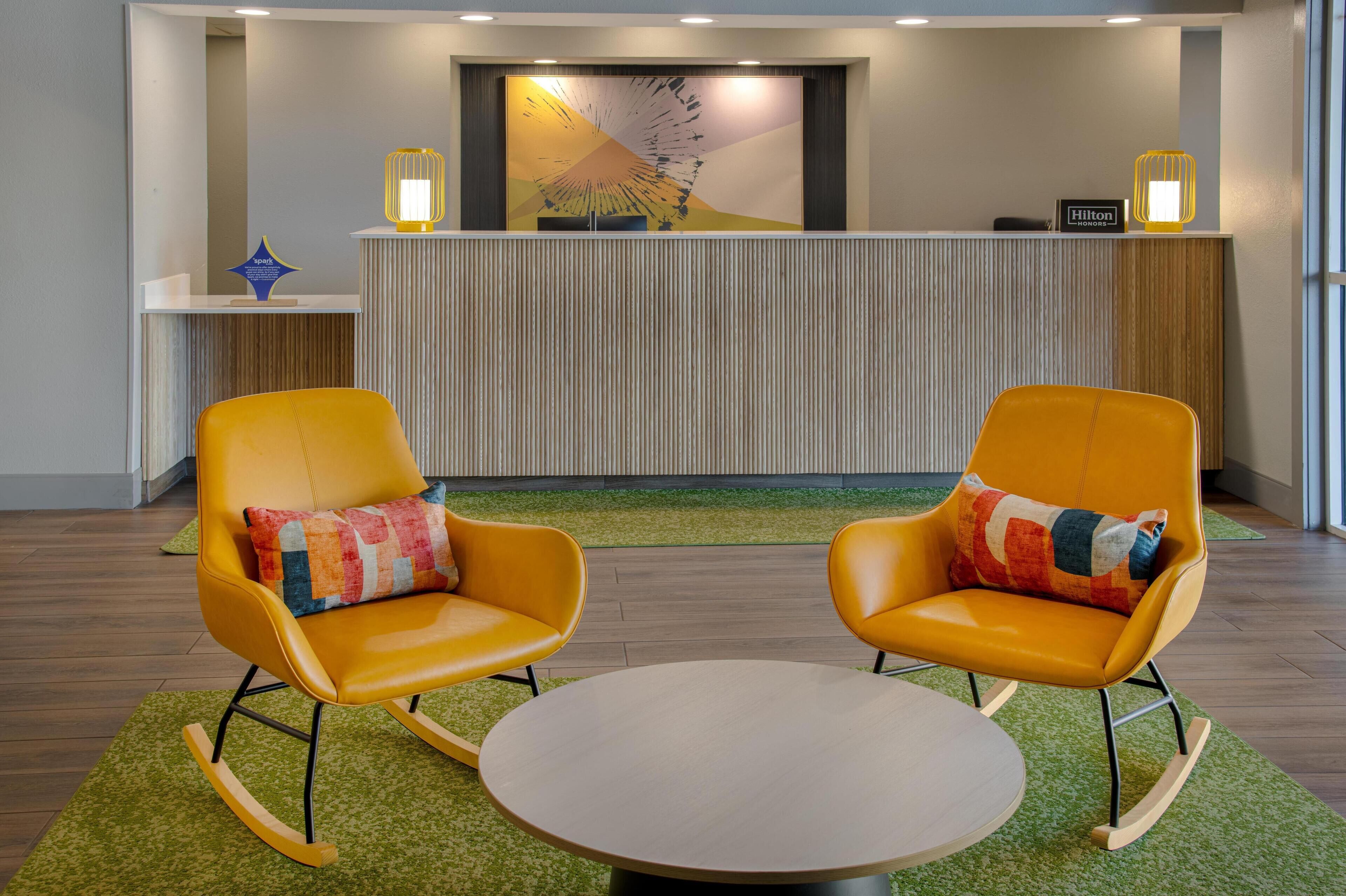 A reception area with a modern design, featuring a reception desk, two rocking chairs with colorful cushions, and a round table.