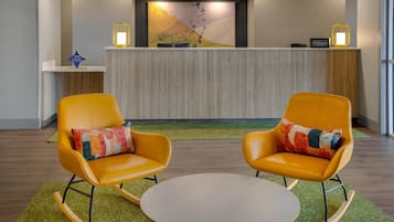 A reception area with a modern design, featuring a reception desk, two rocking chairs with colorful cushions, and a round table.