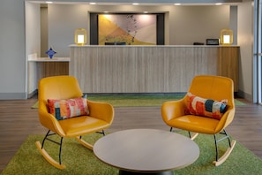 Un área de recepción con diseño moderno, que incluye un mostrador de recepción, dos sillones mecedores con cojines de colores, y una mesa redonda.
