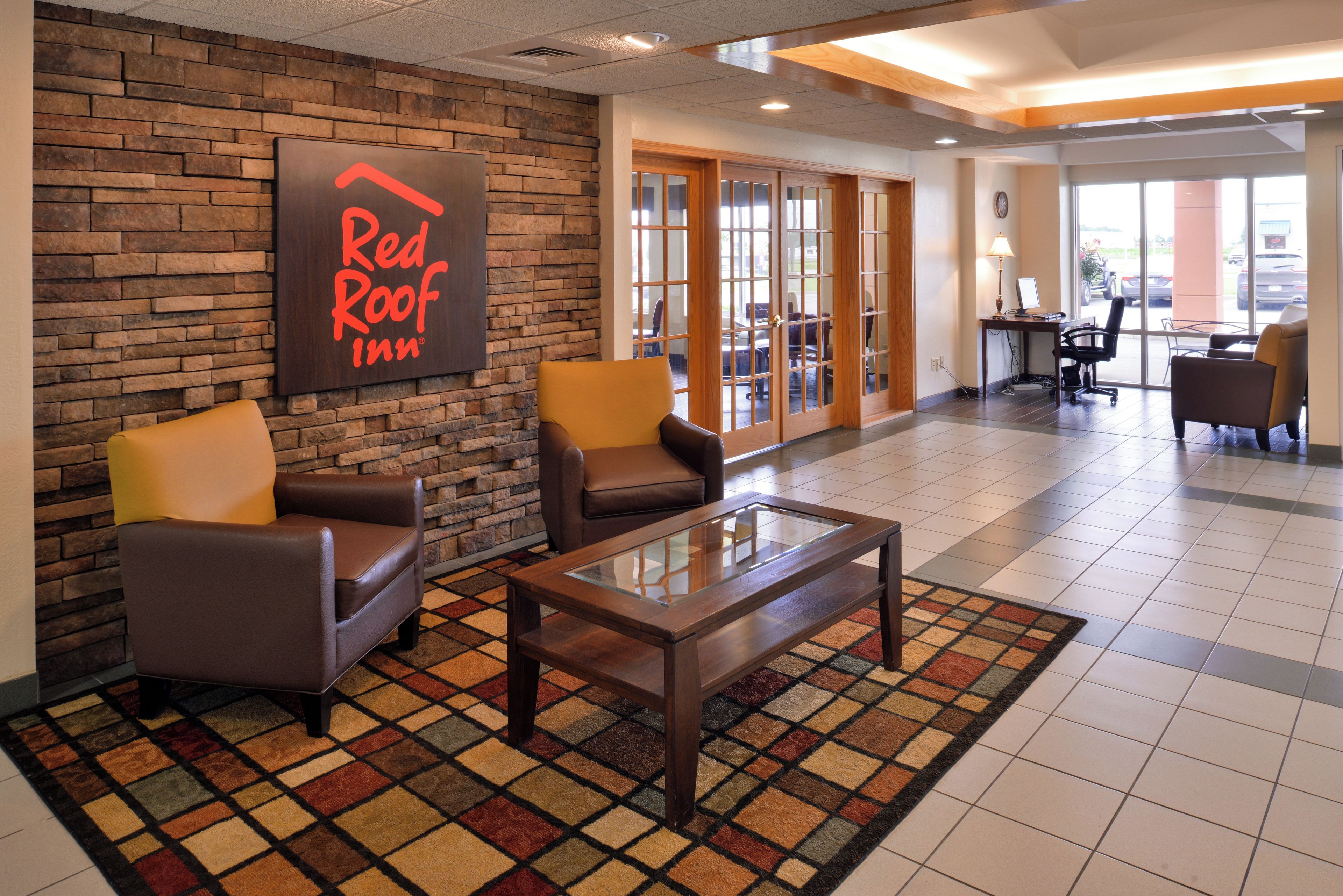 A Red Roof Inn lobby with leather armchairs, a glass-top coffee table, and a stone wall.
