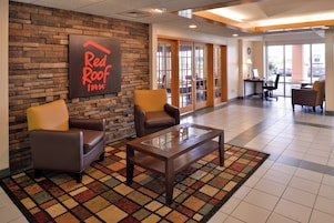 Vestíbulo de Red Roof Inn con sillones de cuero, una mesa de centro de vidrio y una pared de piedra.