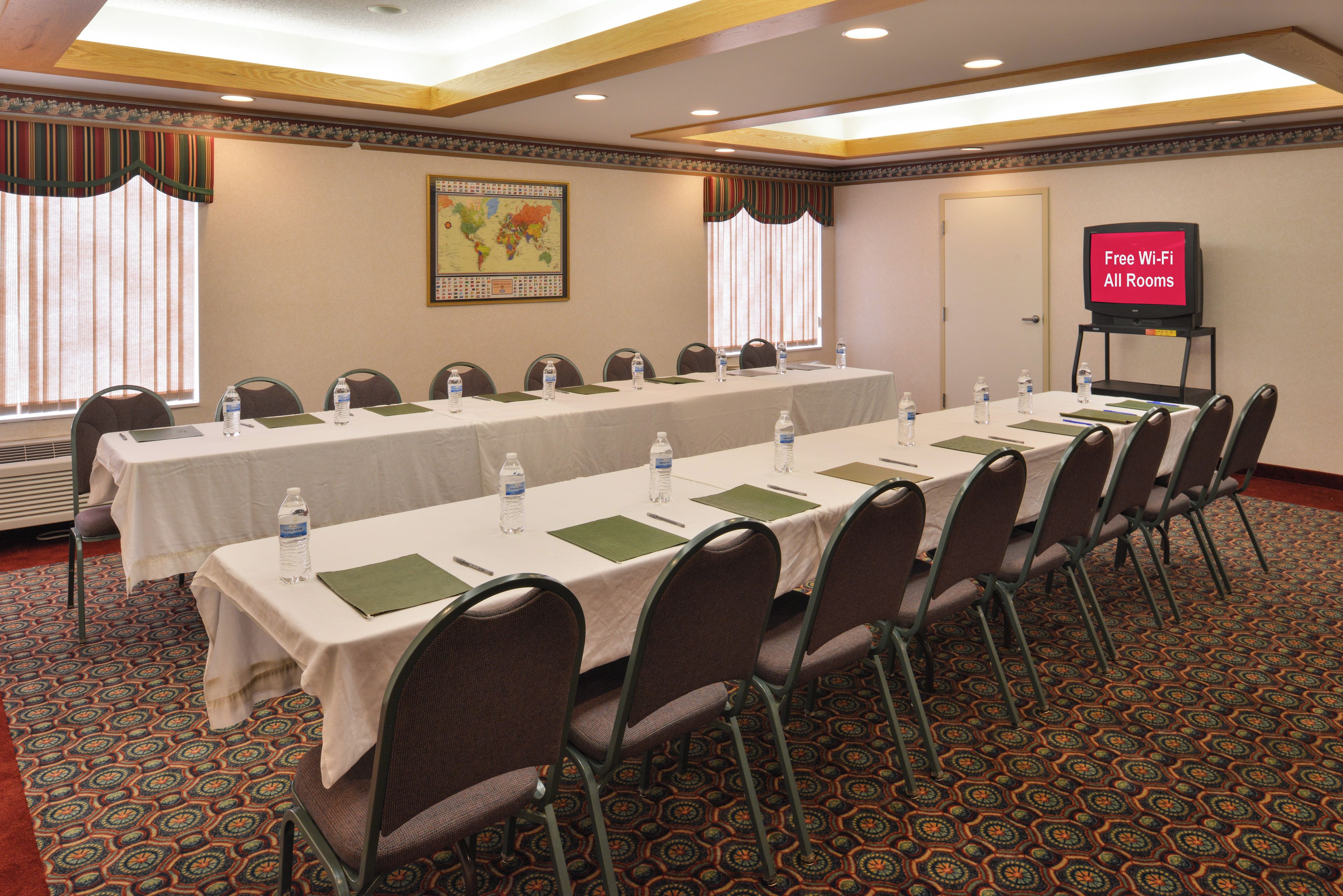 A conference room with a long table, chairs, water bottles, and a television screen indicating free Wi-Fi availability.