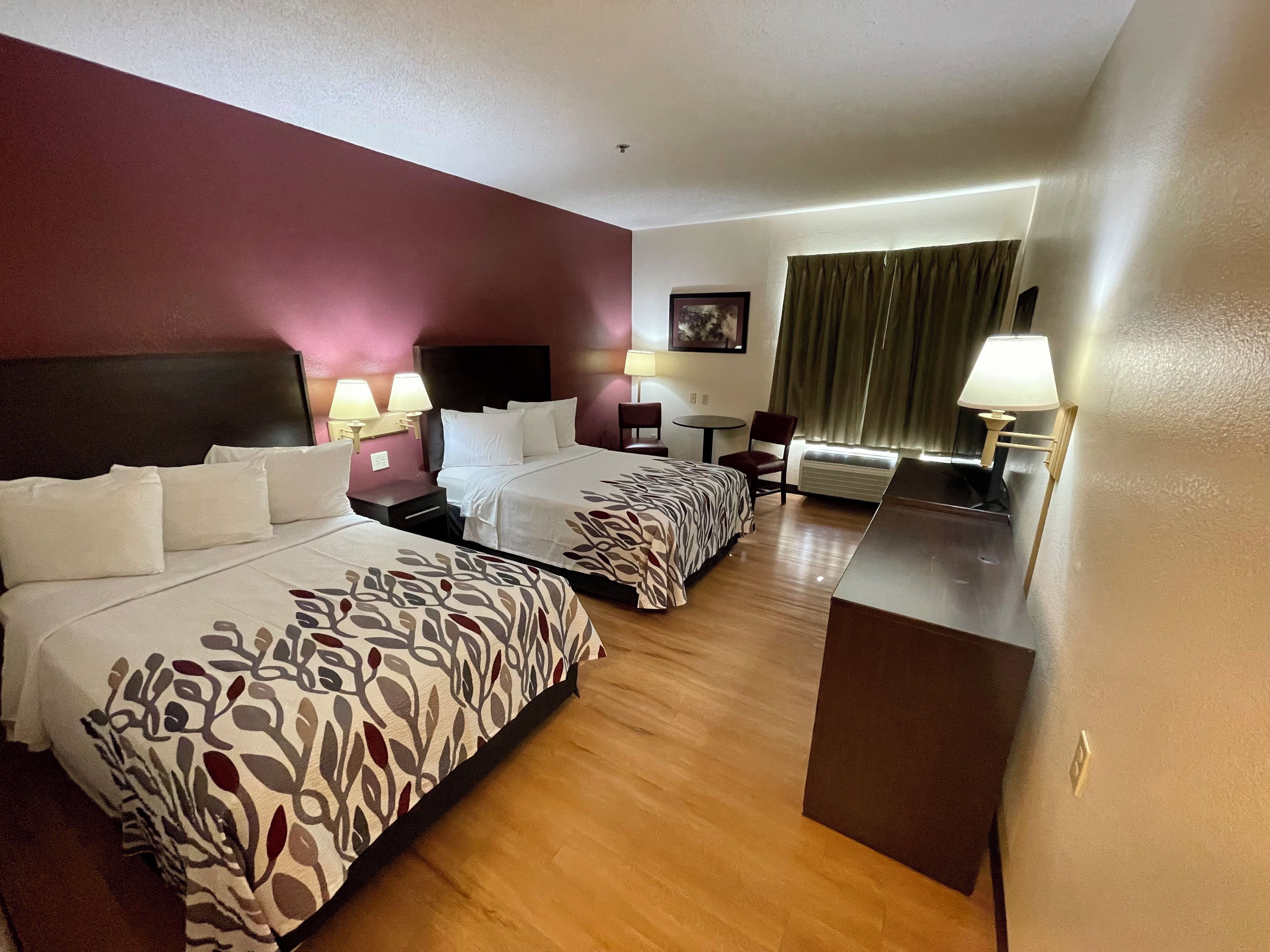 Habitación de hotel con dos camas, un escritorio, una silla, una lámpara y un cuadro en la pared.