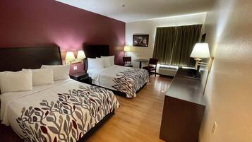 Habitación de hotel con dos camas, un escritorio, una silla, una lámpara y un cuadro en la pared.