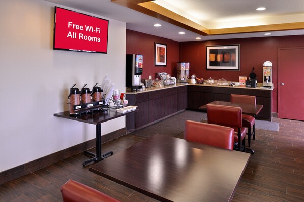 A hotel room with a large TV displaying "Free Wi-Fi All Rooms," a kitchenette with coffee machines, and a seating area with tables and chairs. - Red Roof Inn Clyde (Clyde)