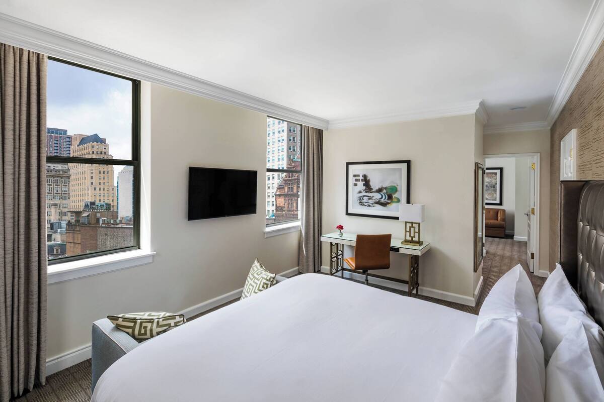 A hotel room with a large bed, a desk, a chair, a TV, and a city view.