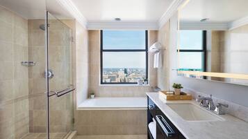 A modern bathroom with a glass-enclosed shower, a bathtub, a large window with a city view, and a vanity with a sink and mirror.