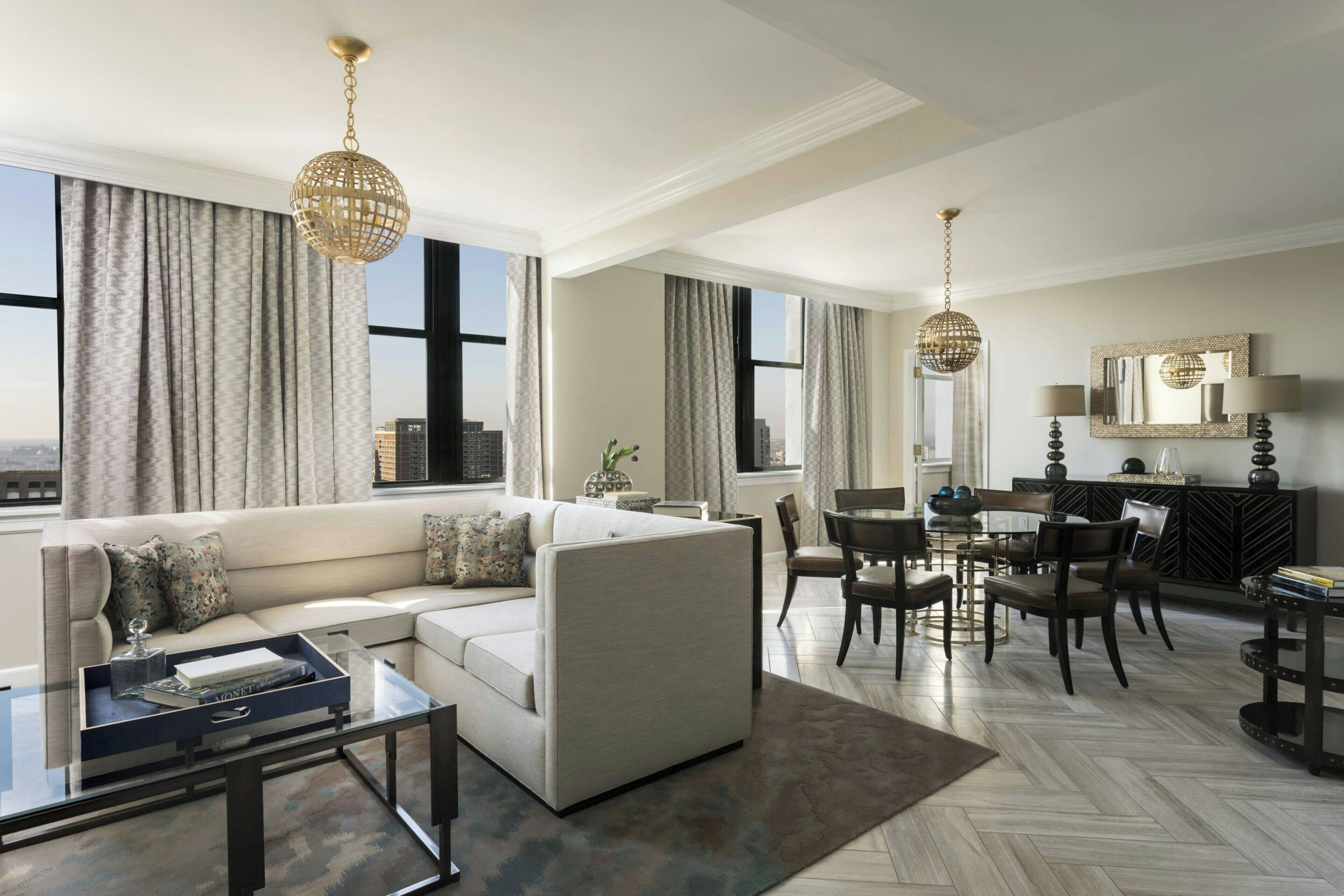 A modern living room with a sectional sofa, a glass coffee table, and a dining area with a chandelier.