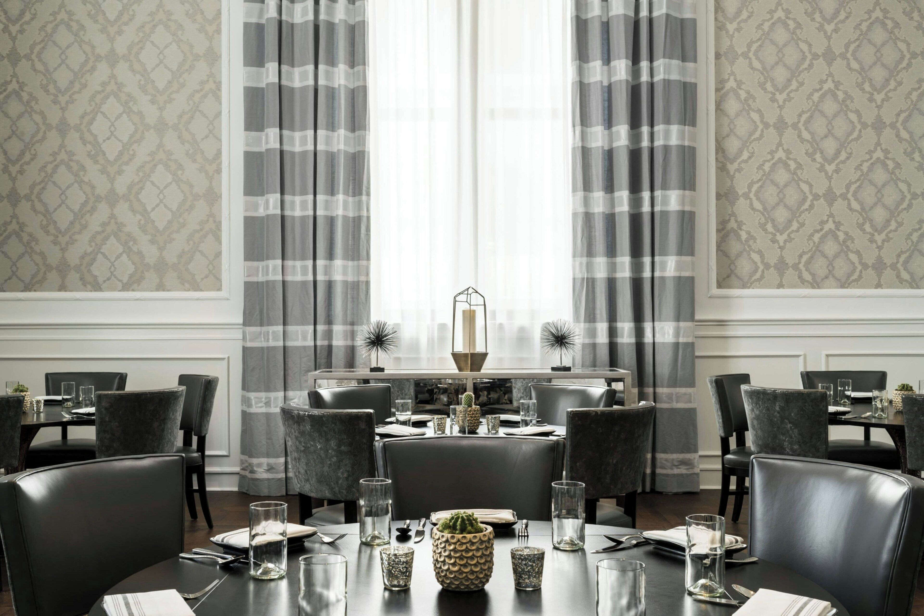 Un coin repas avec une table dressée pour quatre personnes, entourée de chaises, et une grande fenêtre avec des rideaux en arrière-plan.