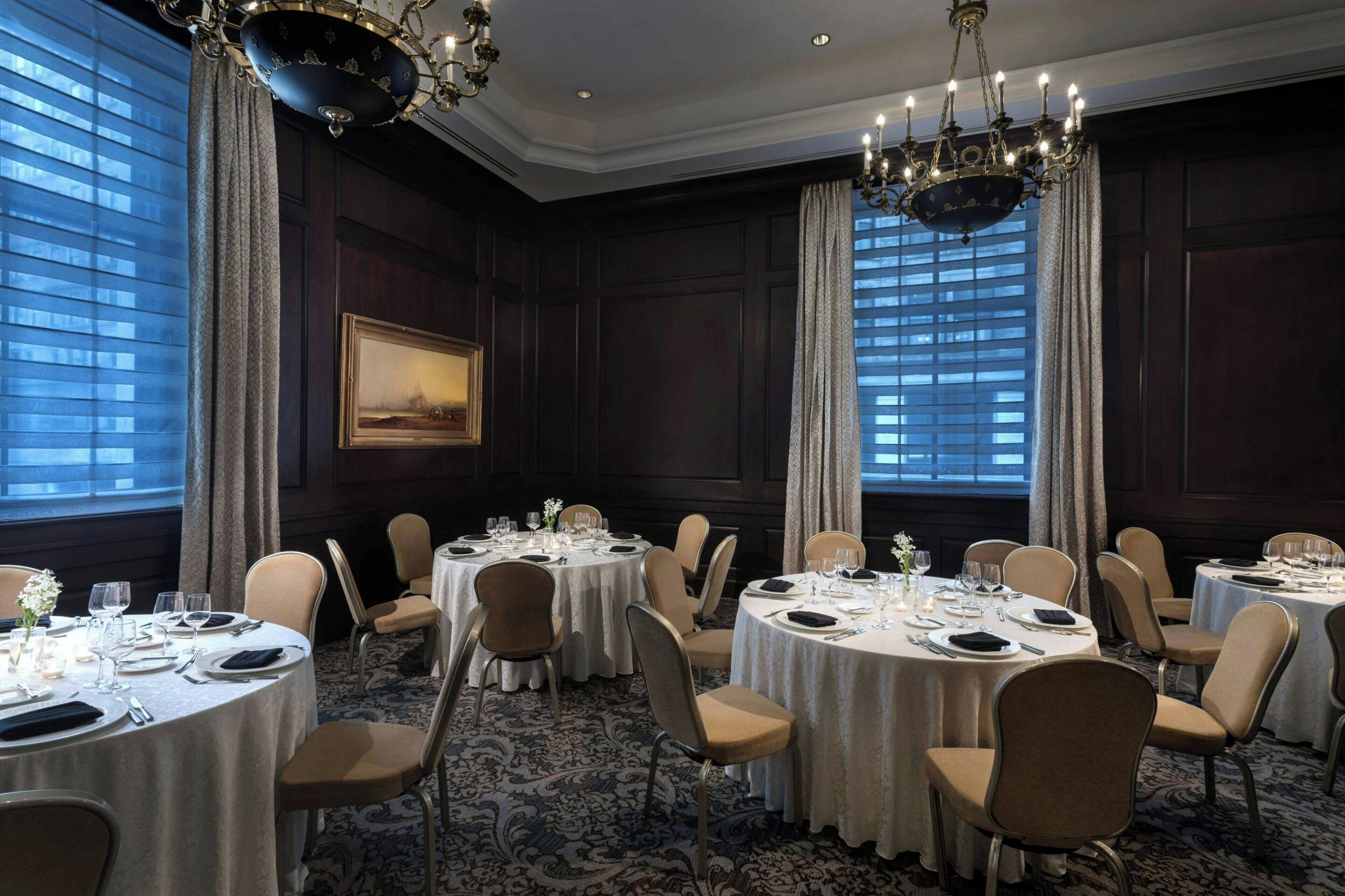 A formal dining room with round tables, chairs, and chandeliers.
