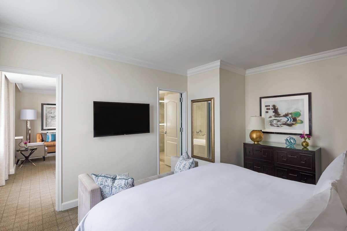 A hotel room with a large bed, a flat-screen TV mounted on the wall, a desk with a lamp, and a dresser with decorative items.