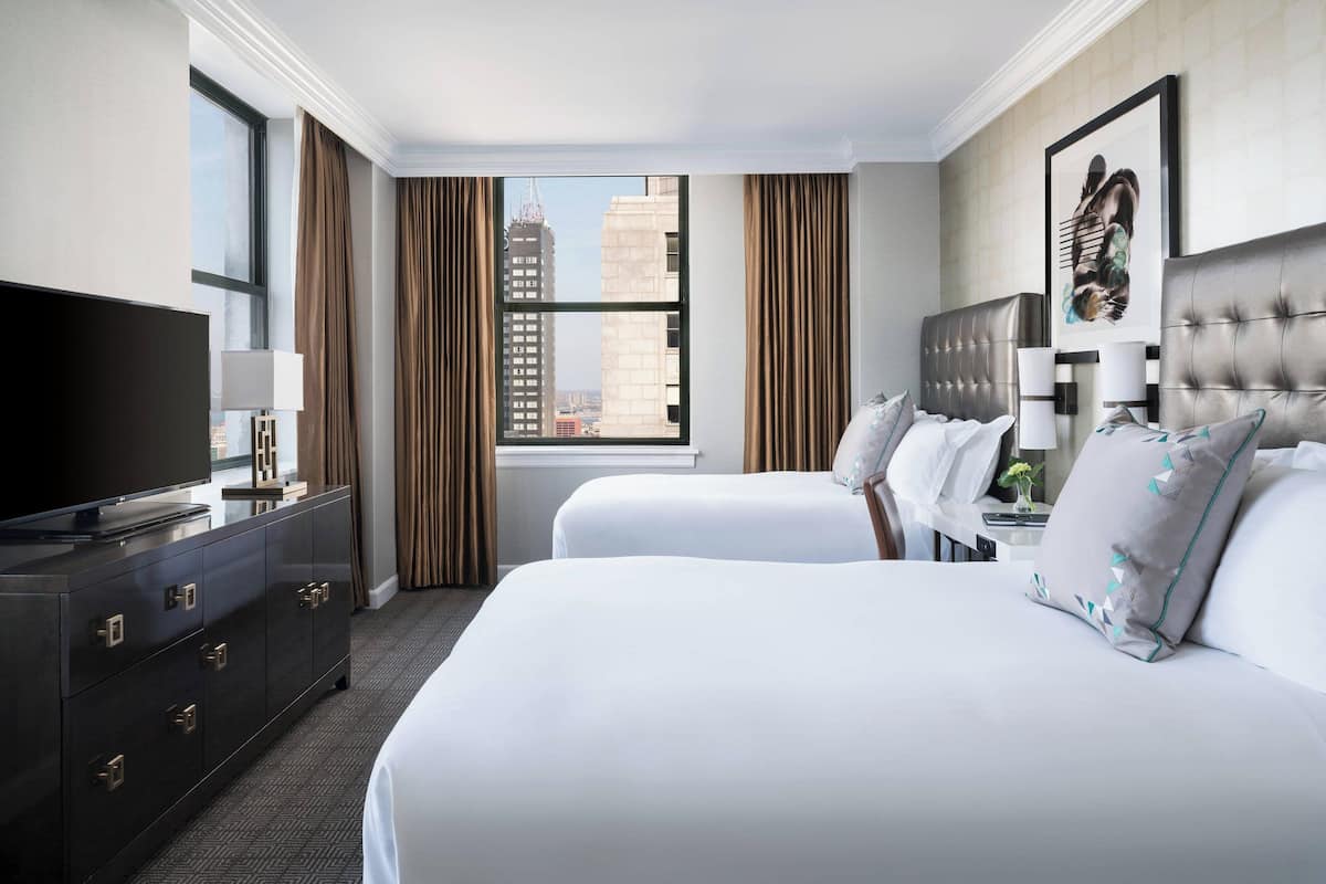 Habitación de hotel con dos camas, televisión, cómoda y ventana con vista a la ciudad.